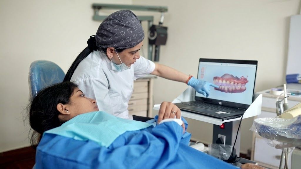 A dentist points to a 3D scan of teeth on a laptop while her patient looks on from the chair