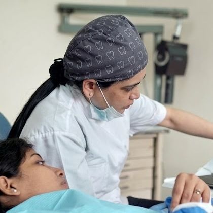 The dentist in her clinic, wearing a white coat and a patterned surgical cap